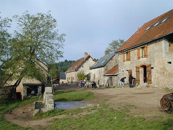 Cour de ferme en pierre avec puits et groupe d'enfants en activité