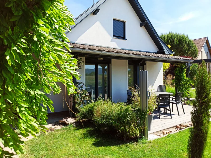 Façade blanche avec jardinet fleuri et terrasse avec chaises de jardin