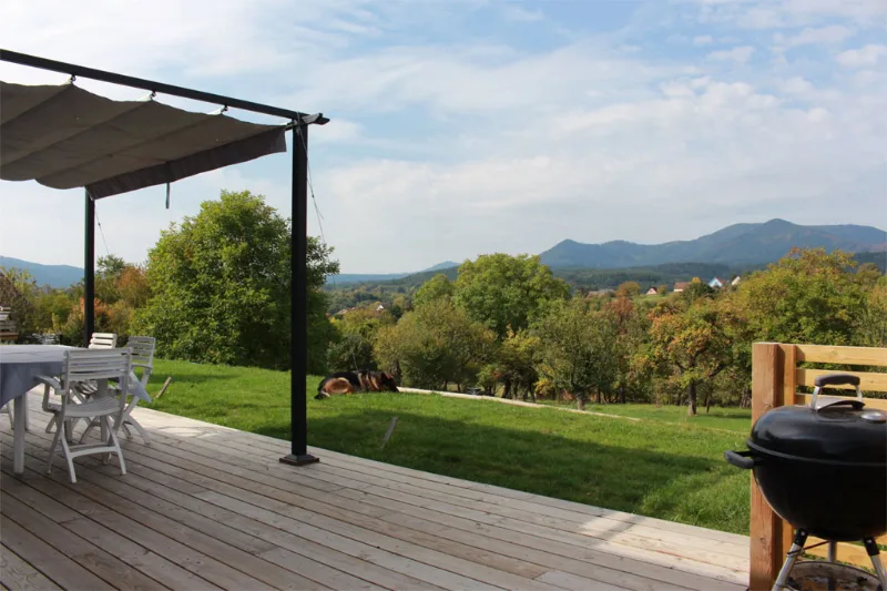 Terrasse bois avec store, barbecue et vue dégagée sur massif vosgien