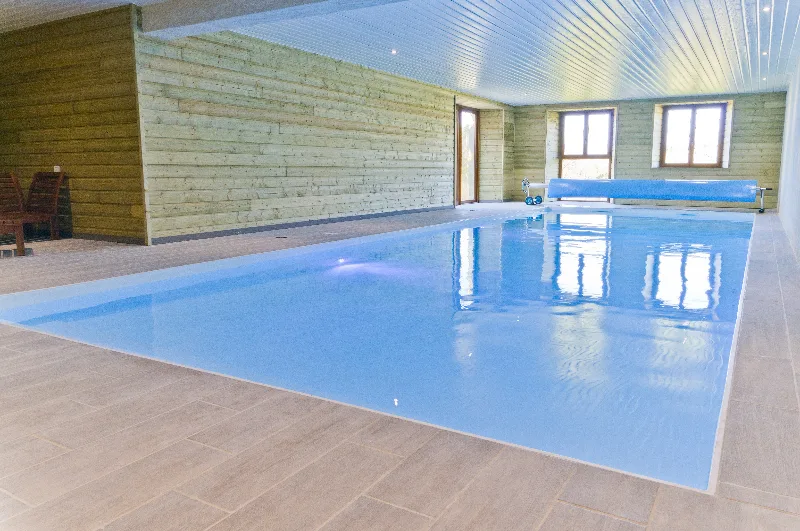Piscine intérieure chauffée au bassin bleu, murs en lambris bois clair et margelle carrelée
