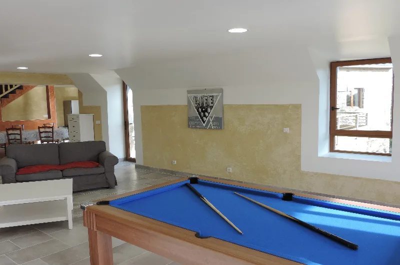 Salle de jeux avec billard au tapis bleu, canapé, coin repas et escalier desservant l'étage