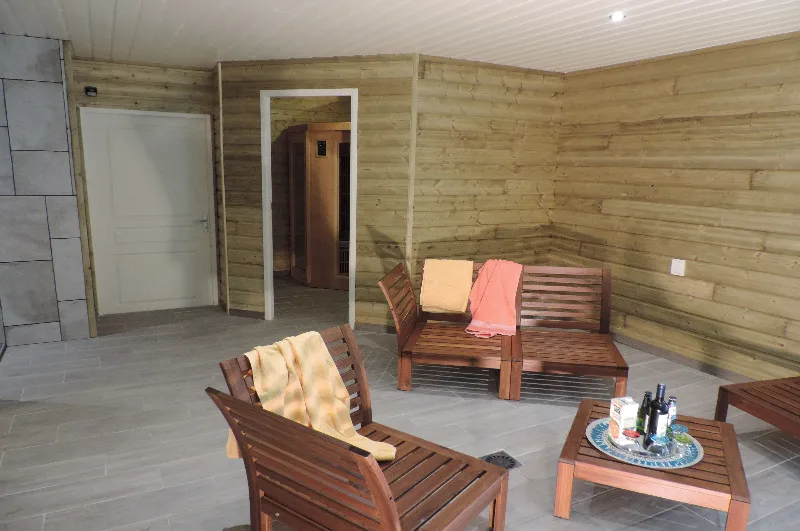 Espace détente lambrissé de bois avec transats, serviettes et table basse, accès à la zone sauna