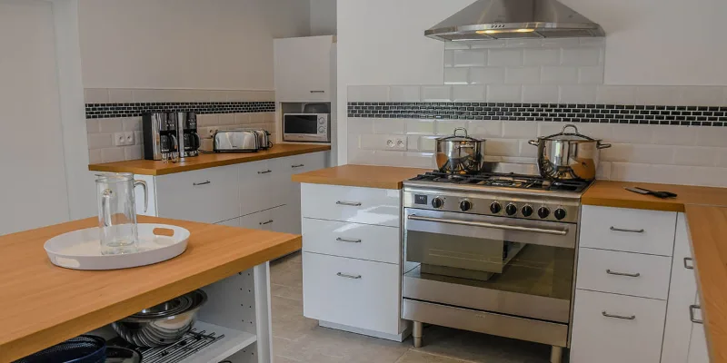 Cuisine spacieuse avec piano de cuisson inox, hotte, îlot bois et électroménager pour grandes tablées