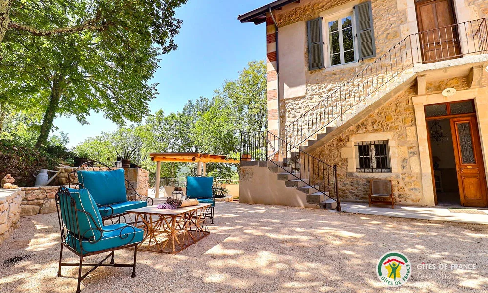Gîte de groupe Domaine des Brugieres à Lagorce — Cour ensoleillee avec salon de jardin colore, pergola et escalier en pierre de la batisse, capacité 24 personnes