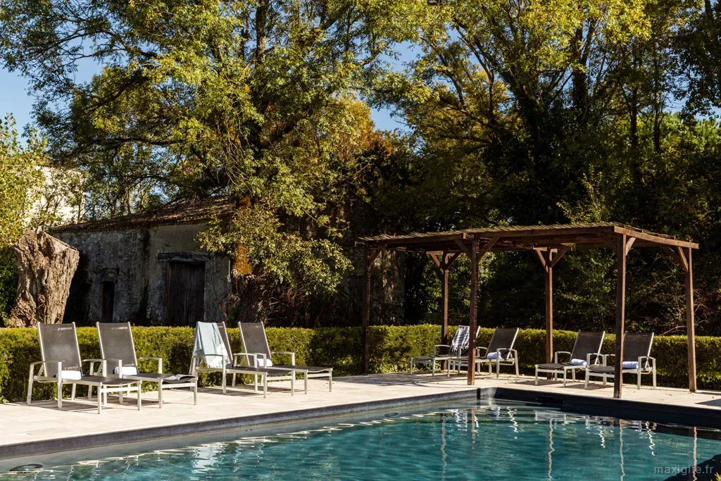 Piscine entouree de transats et pergola en bois, grands arbres offrant de l'ombre
