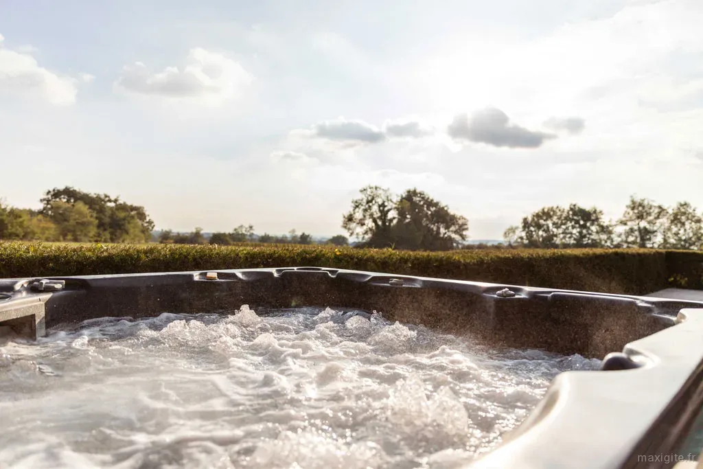 Bain a remous en fonctionnement face a la campagne, haie taillee et arbres a l'horizon