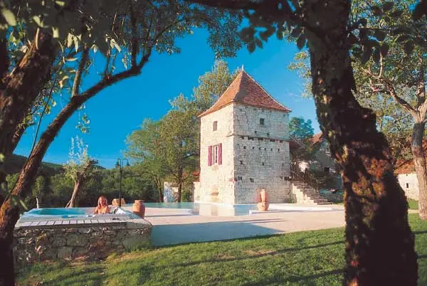 Gîte de groupe Le Hameau des Saveurs à Maxou — Pigeonnier en pierre et bâtisses anciennes dominant la piscine, jardin verdoyant et ciel bleu, capacité 30 personnes