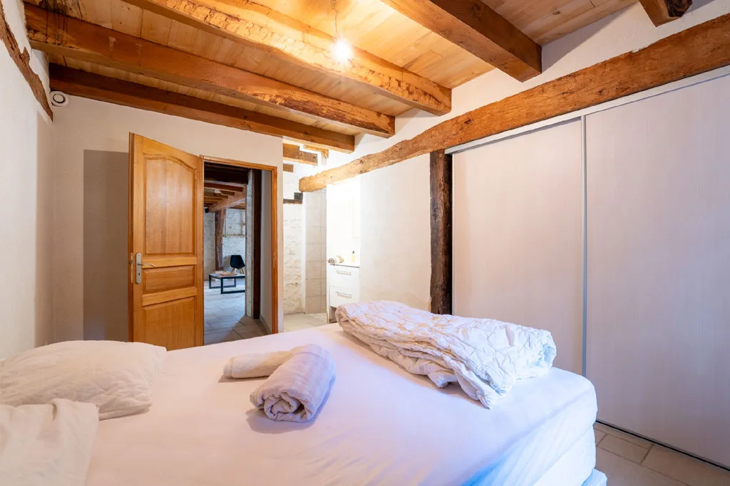 Chambre avec grand lit, poutres anciennes apparentes, placards coulissants et accès à la salle d'eau
