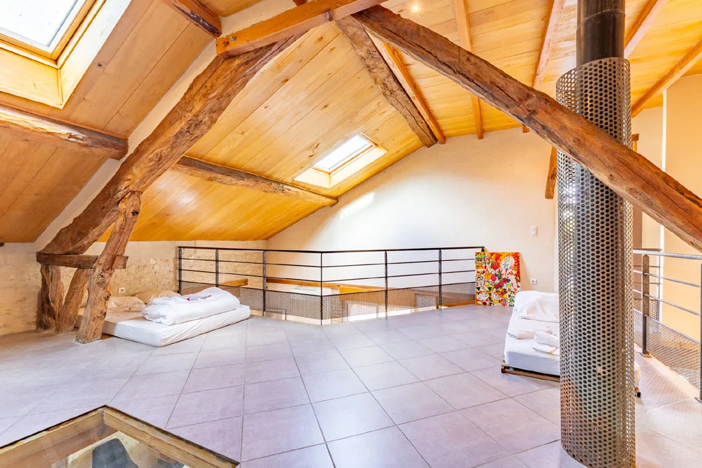 Mezzanine dortoir sous charpente avec matelas au sol et velux, vaste espace nuit collectif