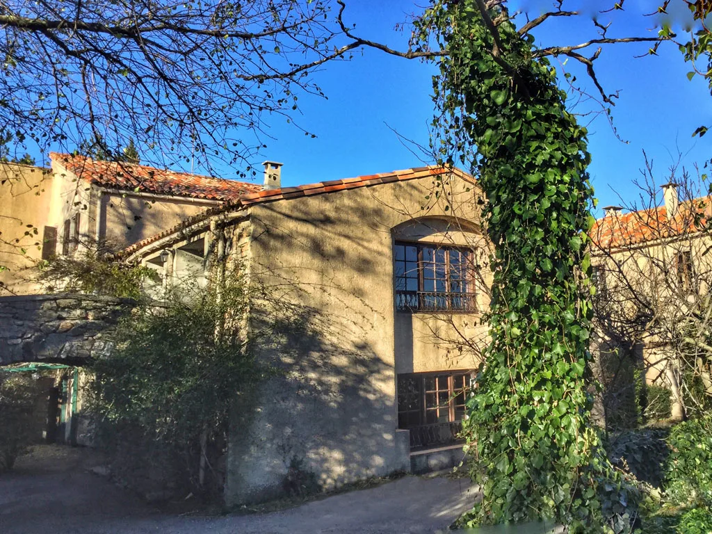 Gîte de groupe Domaine de Lacan à Vélieux — Façade en pierre d'une bâtisse ancienne aux grandes fenêtres cintrées et lierre grimpant, capacité 45 personnes