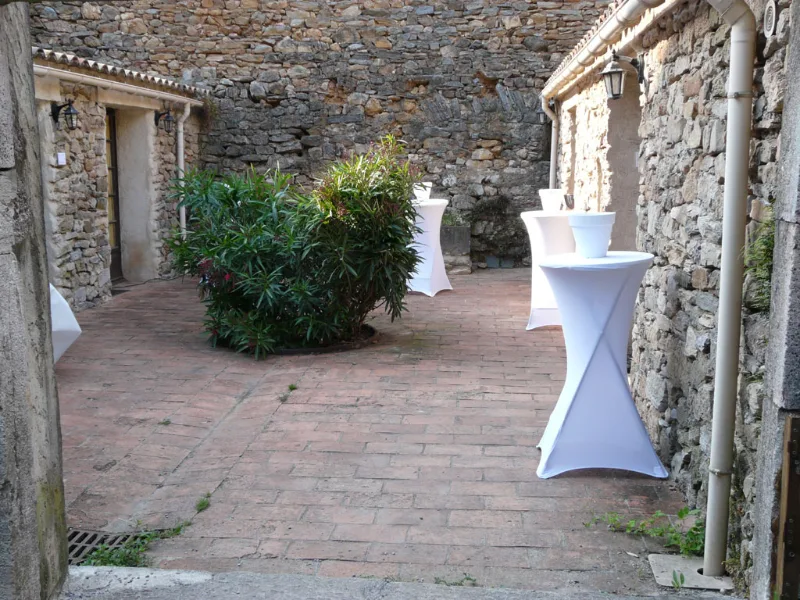 Cour pavée close de murs en pierre avec mange-debout habillés de blanc pour réception