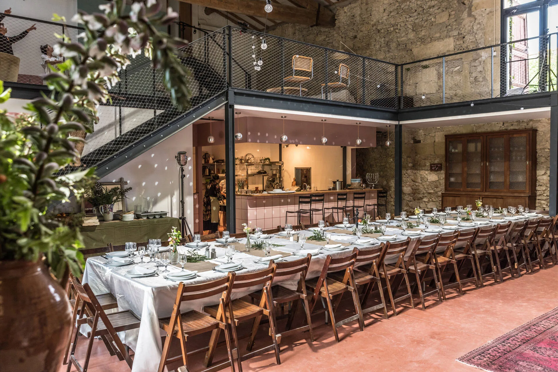 Gîte de groupe Domaine Sesquier à Mèze — Grande salle voûtée en pierre avec longue tablée dressée, mezzanine et cuisine ouverte au fond, capacité 37 personnes