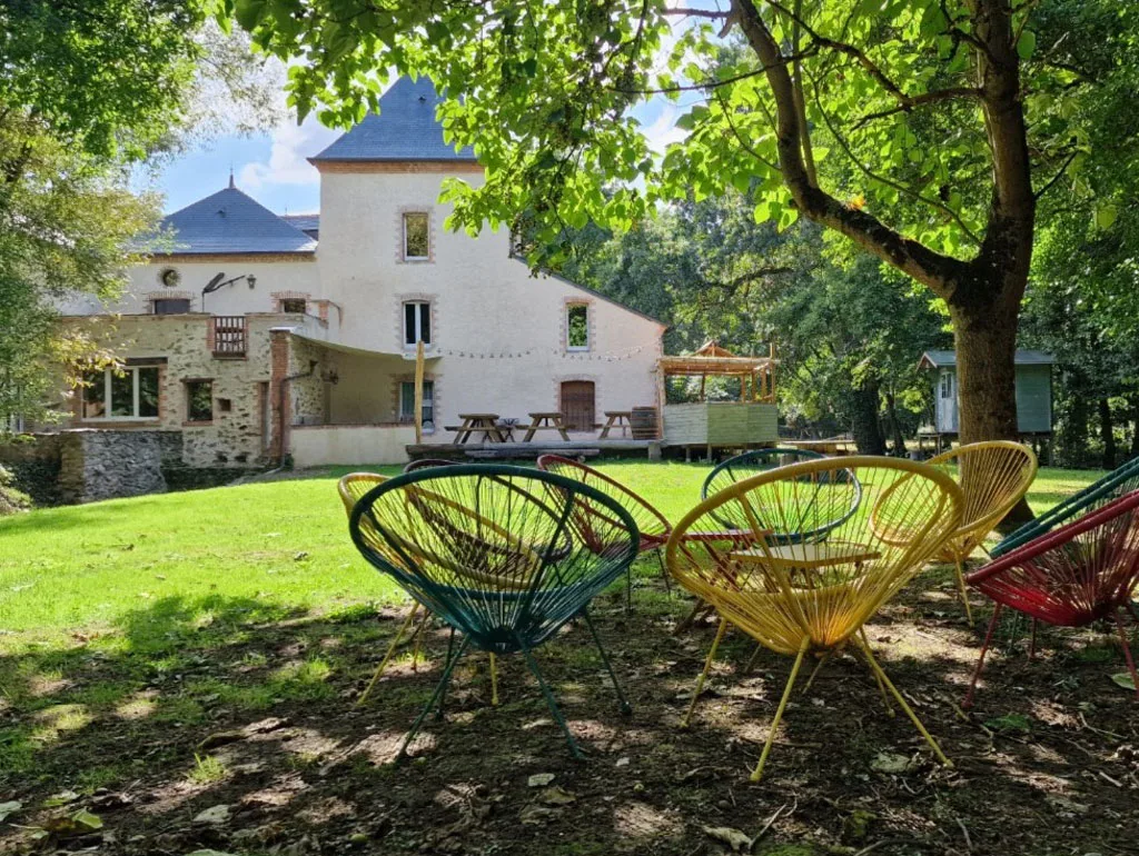 Gîte de groupe Moulin du Chapitre à Chanzeaux — Fauteuils colorés sur pelouse face à une villa bourgeoise en pierre, capacité 28 personnes