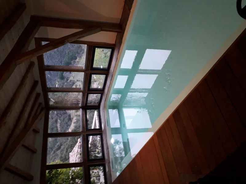 Piscine intérieure sous charpente bois avec verrière et vue sur vallon boisé