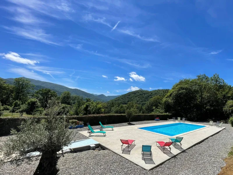 Piscine et transats colorés sous grand ciel bleu avec panorama sur montagnes verdoyantes