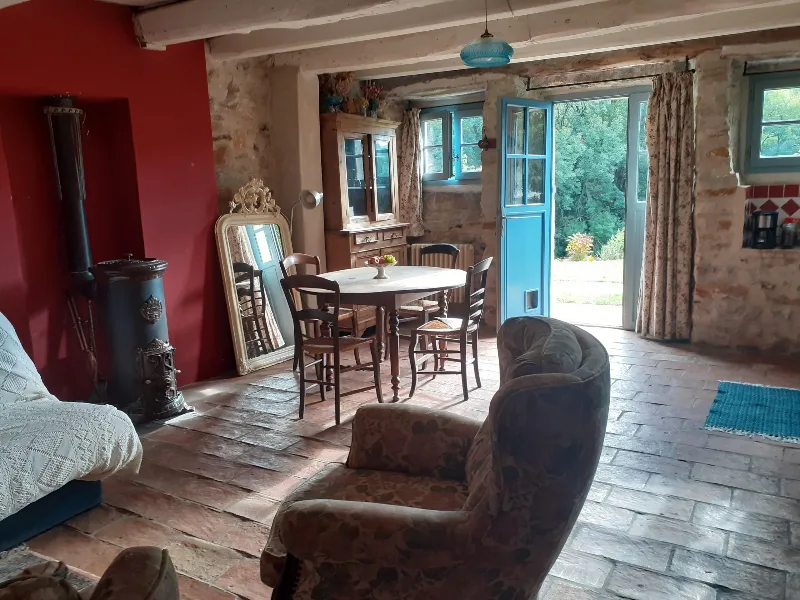 Grande pièce à vivre voûtée en pierre avec table en bois, cheminée et porte-fenêtre ouverte sur le jardin