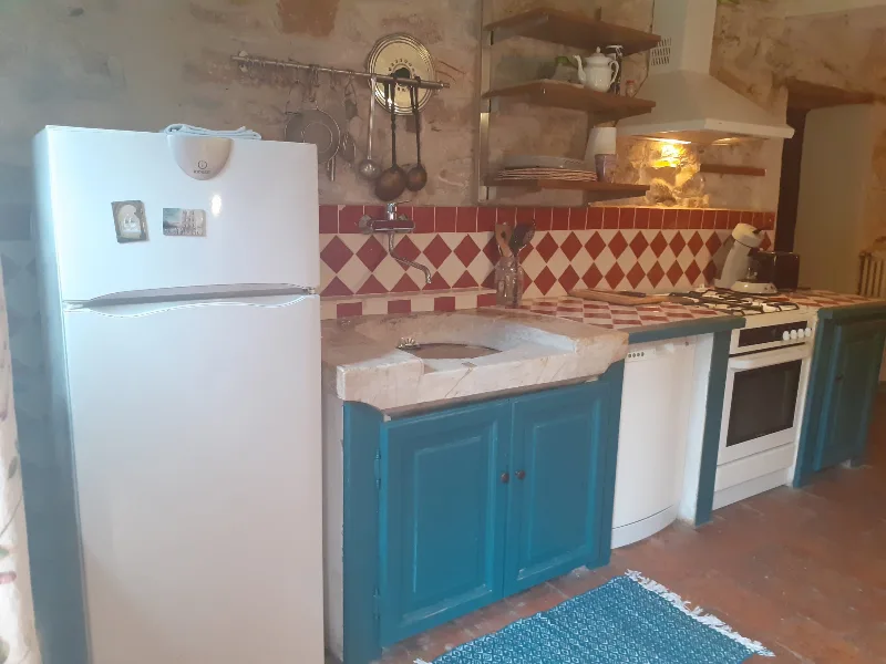 Cuisine traditionnelle en pierre avec meubles bleus, crédence à damier rouge et blanc et ustensiles suspendus