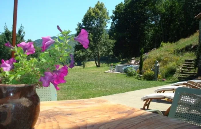Jardin en terrasse avec bassin de baignade, chaises longues et vue sur la vallée boisée