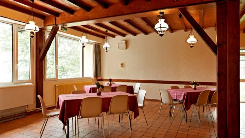 Salle à manger commune aux poutres apparentes, tables dressées et suspensions lumineuses façon lanterne
