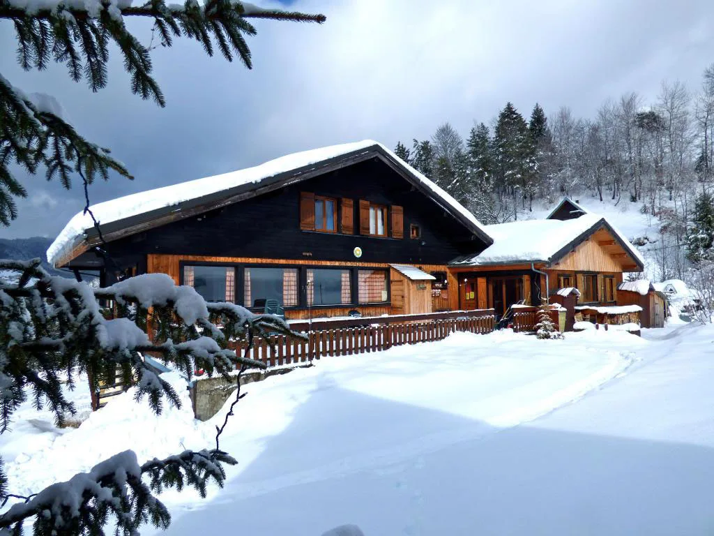 Gîte de groupe Chalet de la Hulotte à Entremont-le-Vieux — Chalet en bois avec toit enneigé et sapins givrés sous ciel couvert, façade boisée, capacité 35 personnes