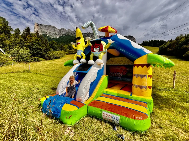 Château gonflable coloré avec toboggan sur pelouse, falaises de Chartreuse en fond