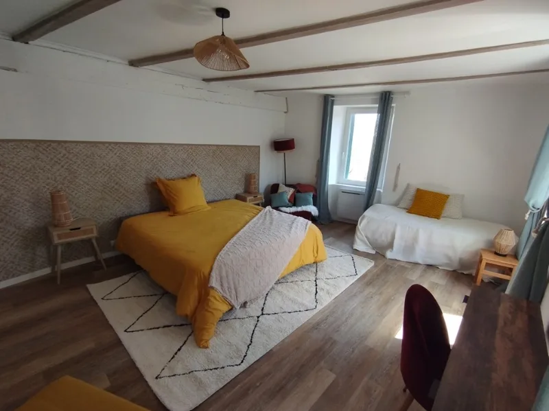 Chambre lumineuse sous poutres apparentes avec parure de lit jaune moutarde et coin salon