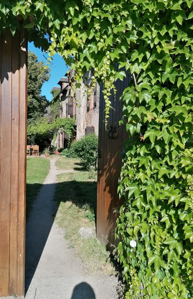 Gîte de groupe L'Arche d'Yvann à Campuac — Portail de bois enlacé de lierre ouvrant sur le jardin de L'Arche d'Yvann à Campuac, capacité 25 personnes