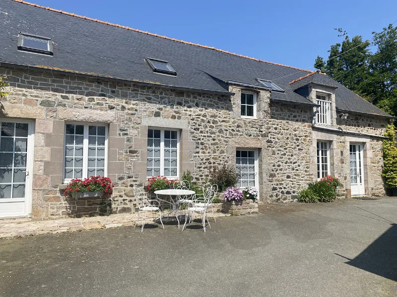 Façade en pierre de la longère avec jardin fleuri et ciel bleu