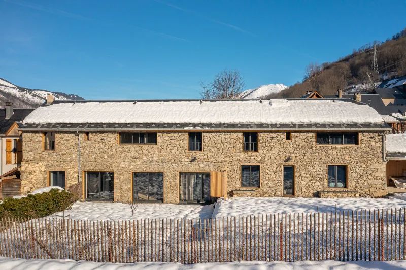 Façade en pierre du chalet sous ciel bleu avec vue sur les sommets pyrénéens enneigés