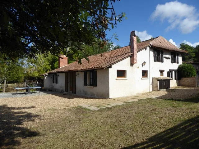 Façade ensoleillée de la maison périgourdine avec volets bleus et jardin arboré