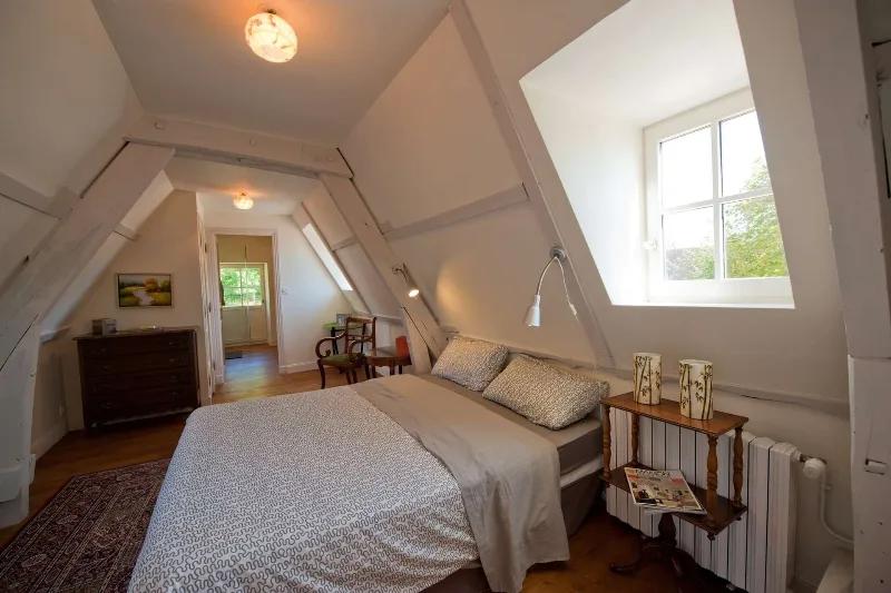 Chambre mansardée lumineuse avec poutres apparentes et fenêtre sur la campagne