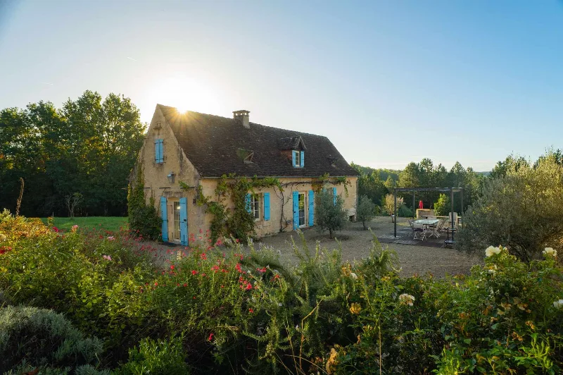 Façade en pierre du gîte aux volets bleus typiques du Périgord, éclairée par le soleil couchant