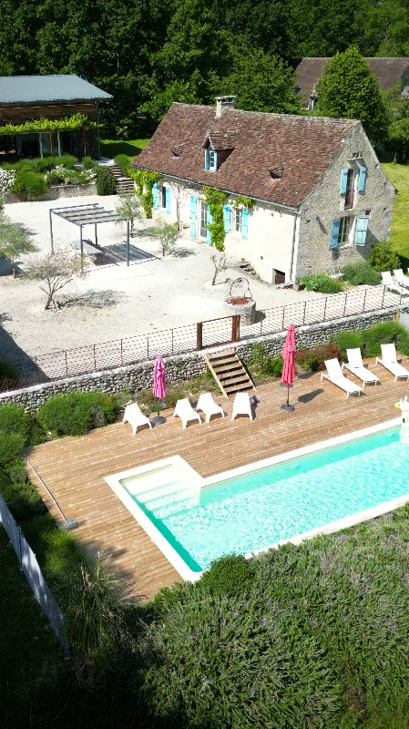Piscine extérieure vue du ciel avec terrasse en bois, transats et jardin arboré