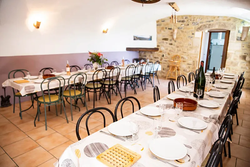 Grande salle à manger voûtée en pierre avec longues tables dressées pour un repas de groupe