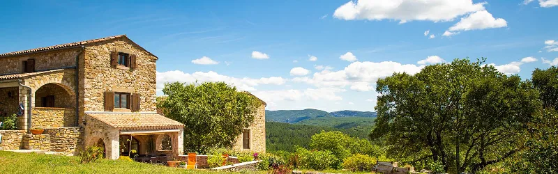 Façade en pierre du gîte avec terrasse couverte et vue sur les collines ardéchoises