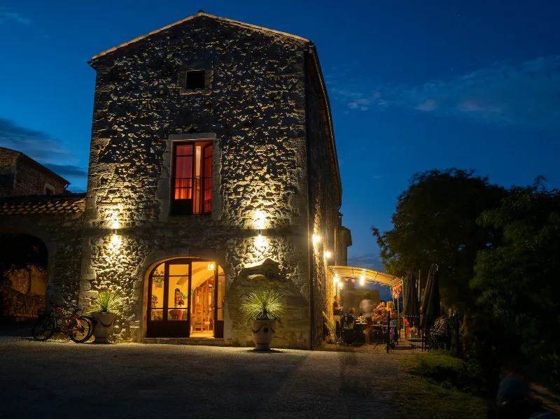 Façade du gîte illuminée à la tombée de la nuit avec fenêtres éclairées