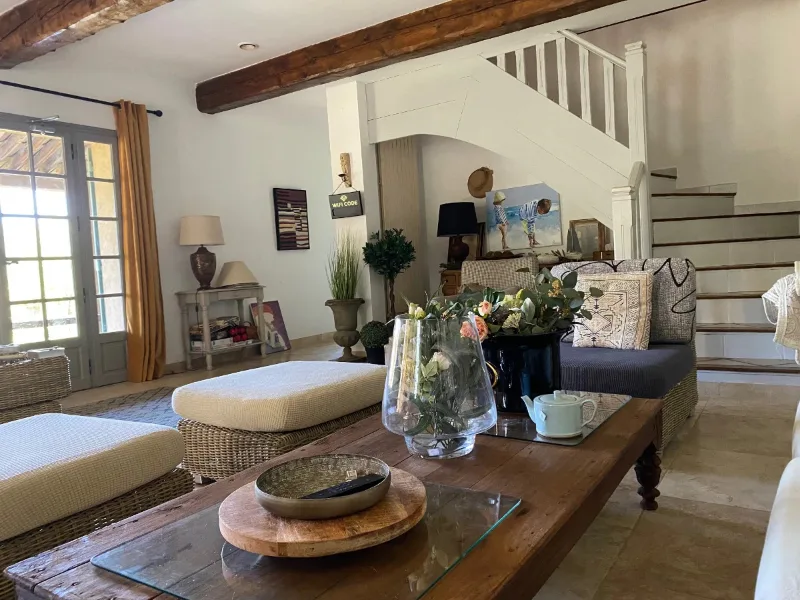 Grand salon avec poutres apparentes, canapés et escalier en bois menant à l'étage