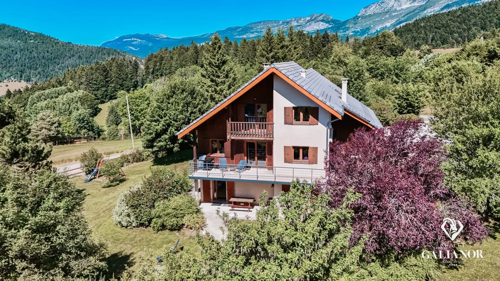 Gîte de groupe Chalet Galianor à Villard-de-Lans — Vue aérienne d'été du chalet en bois avec toit ardoise, entouré de forêt et sommets du Vercors, capacité 24 personnes