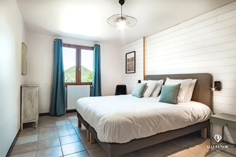 Chambre double lumineuse avec tête de lit capitonnée grise et coussins bleus
