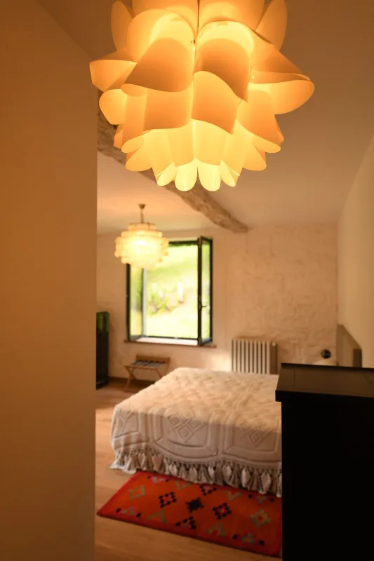 Chambre lumineuse avec grand lit, suspension design et fenêtre sur la campagne