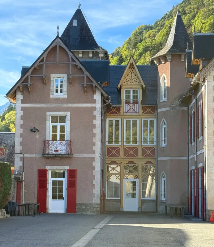 Façade du Château Rolland avec ses tourelles et sa toiture d'ardoise face à la montagne