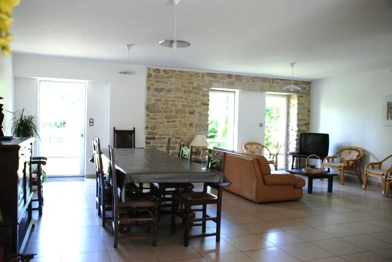 Salon avec mur en pierres apparentes, canapés en cuir et grandes baies vitrées donnant sur le jardin