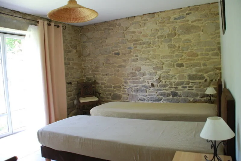 Chambre avec mur en pierres apparentes, deux lits jumeaux et rideaux roses devant la fenêtre