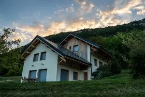 Gîte de groupe Chalets de la Source et des Écureuils à Montagnole — Chalet en bois et crépi blanc au coucher de soleil, niché au pied de la montagne de Chartreuse, capacité 20 personnes