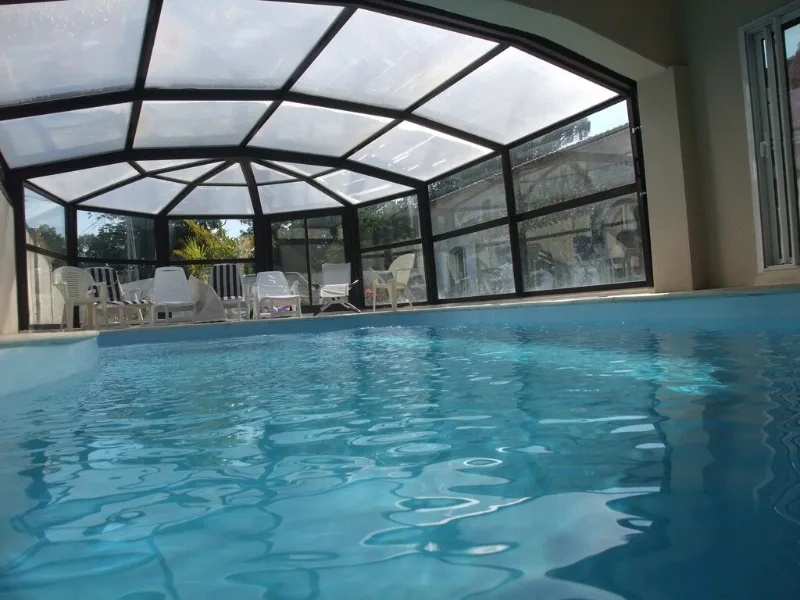 Piscine intérieure chauffée sous véranda avec transats et vue sur le jardin