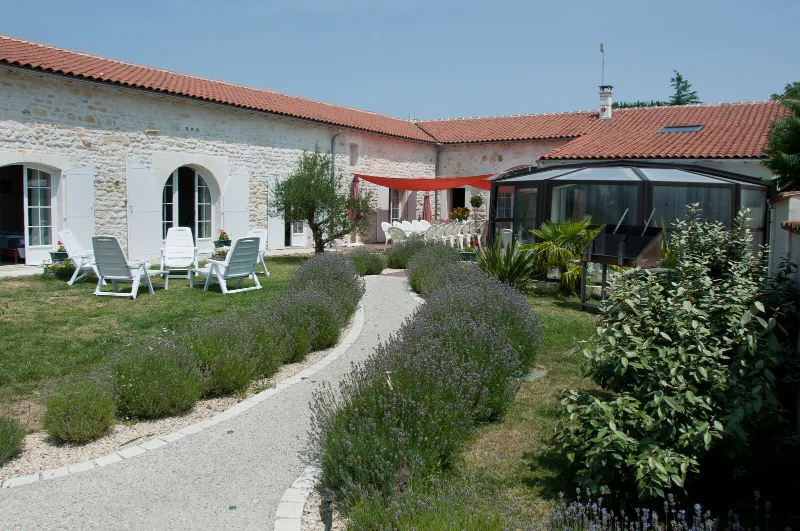 Façade en pierre de l'ancienne ferme charentaise avec jardin de lavande et véranda vitrée