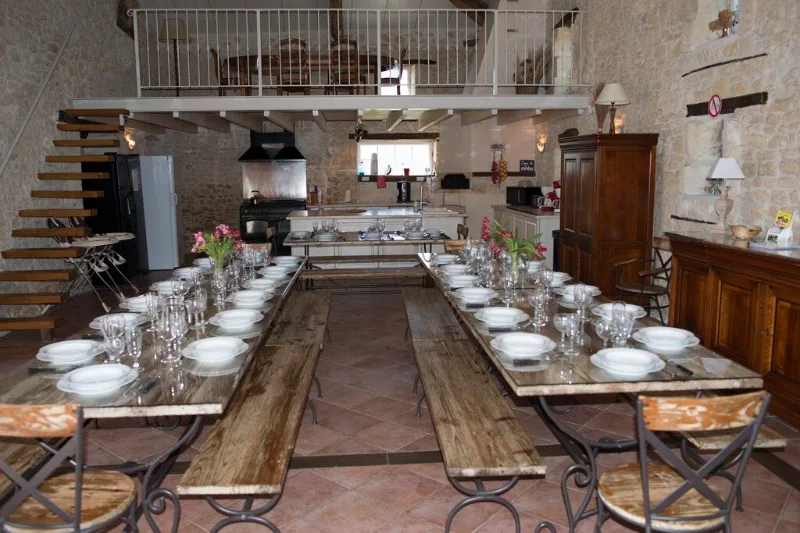 Grande salle de réception aux poutres apparentes avec longues tables dressées et mezzanine