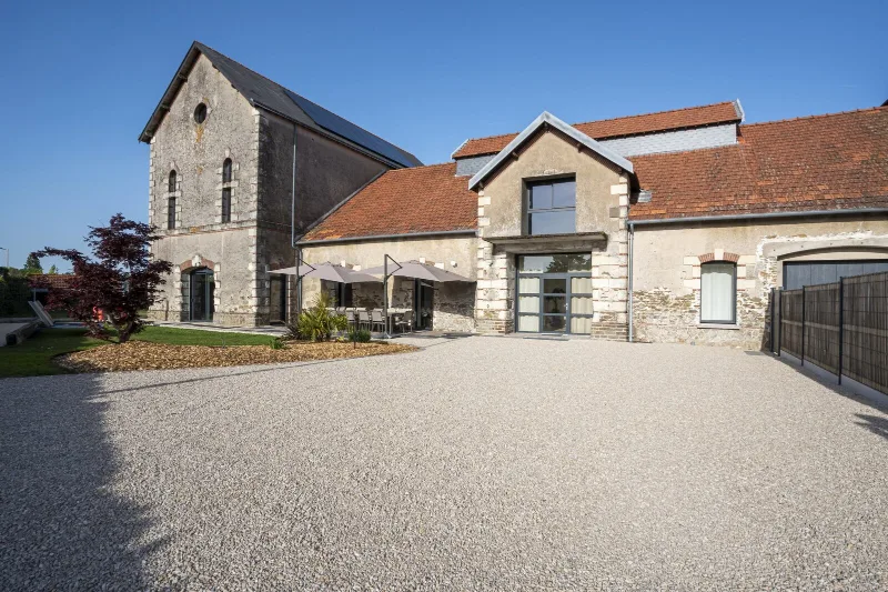 Facade en pierre du corps de ferme renove avec grande cour gravillonnee