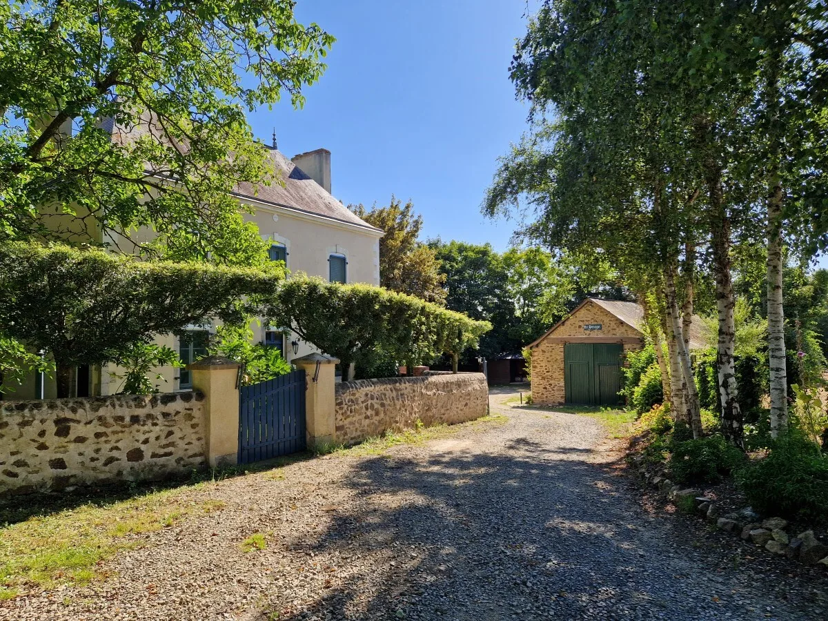 Gîte de groupe La Petite Couannière à Beaulieu-sur-Oudon — Facade en pierre du domaine avec allee gravillonnee et dependance en pierre, capacité 15 personnes