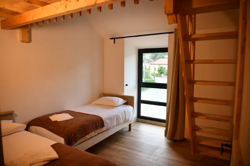 Chambre en mezzanine avec échelle en bois et fenêtre donnant sur le village